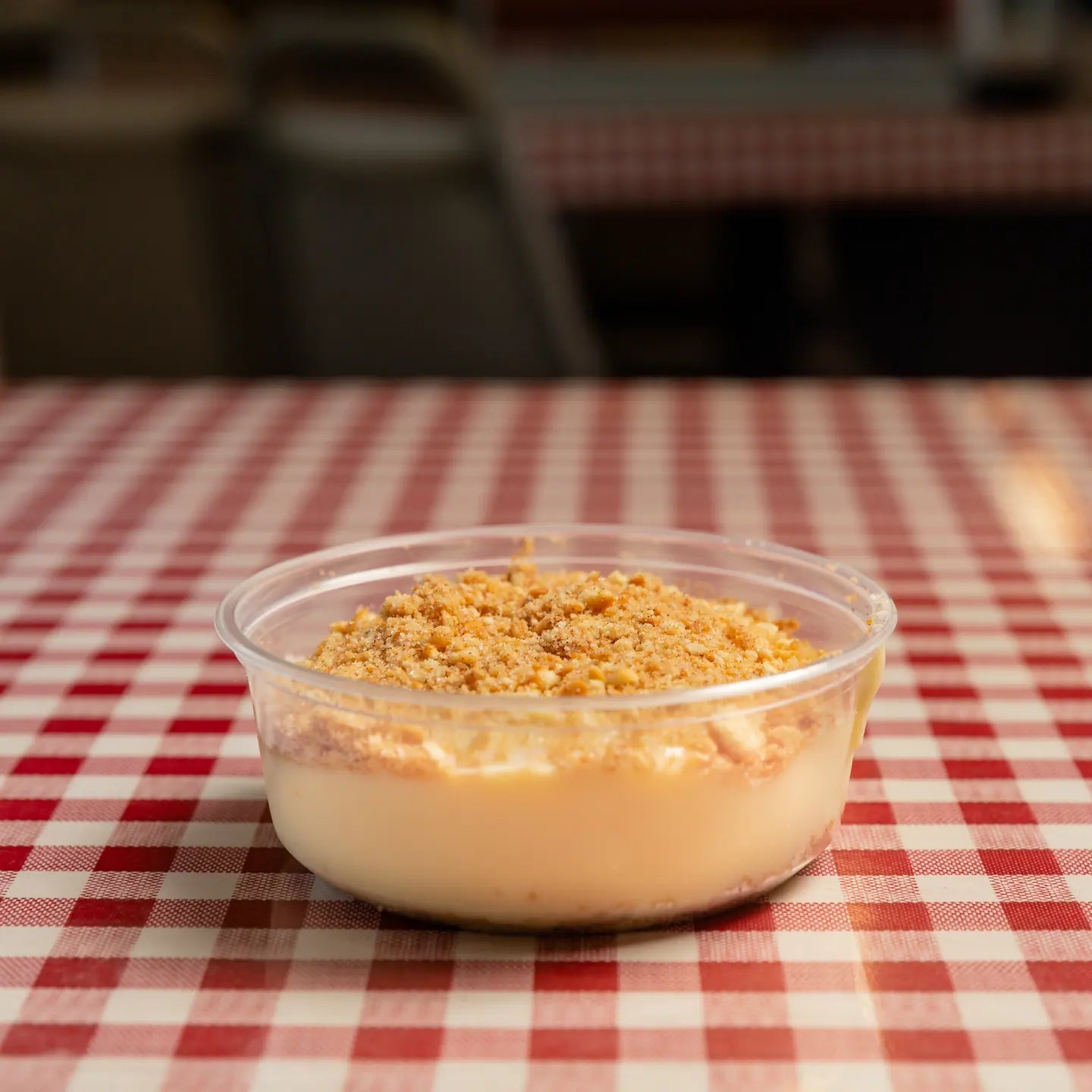 A cup of banana pudding topped with crushed wafers on a red gingham table