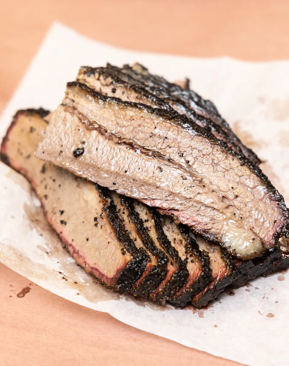 Sliced brisket fanned out on butcher paper, photographed from above, bark and smoke ring showing along every slice