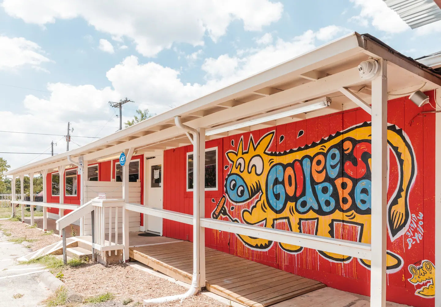 Goldee's red building on Dick Price Road, its painted Goldee's BBQ mural facing the lot under a blue sky
