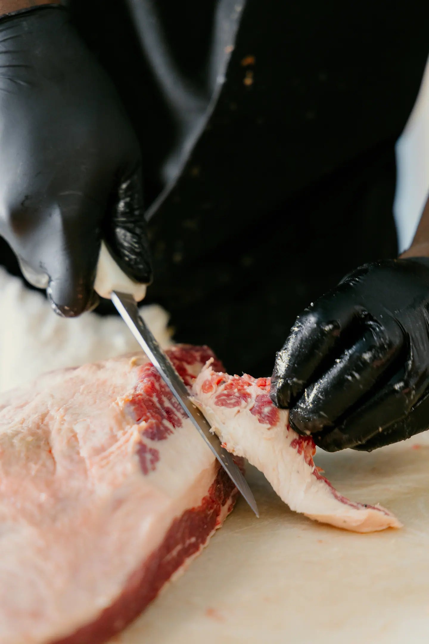 A knife trimming fat from a raw cut on the block