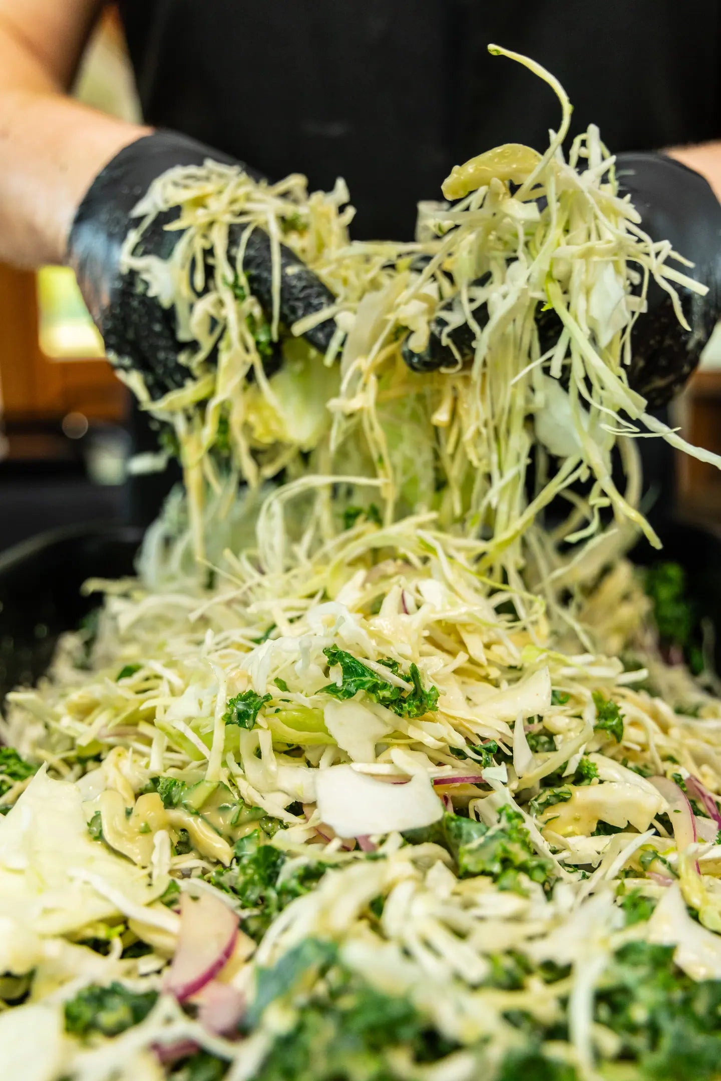 Lemon kale slaw being tossed by hand in a steel pan