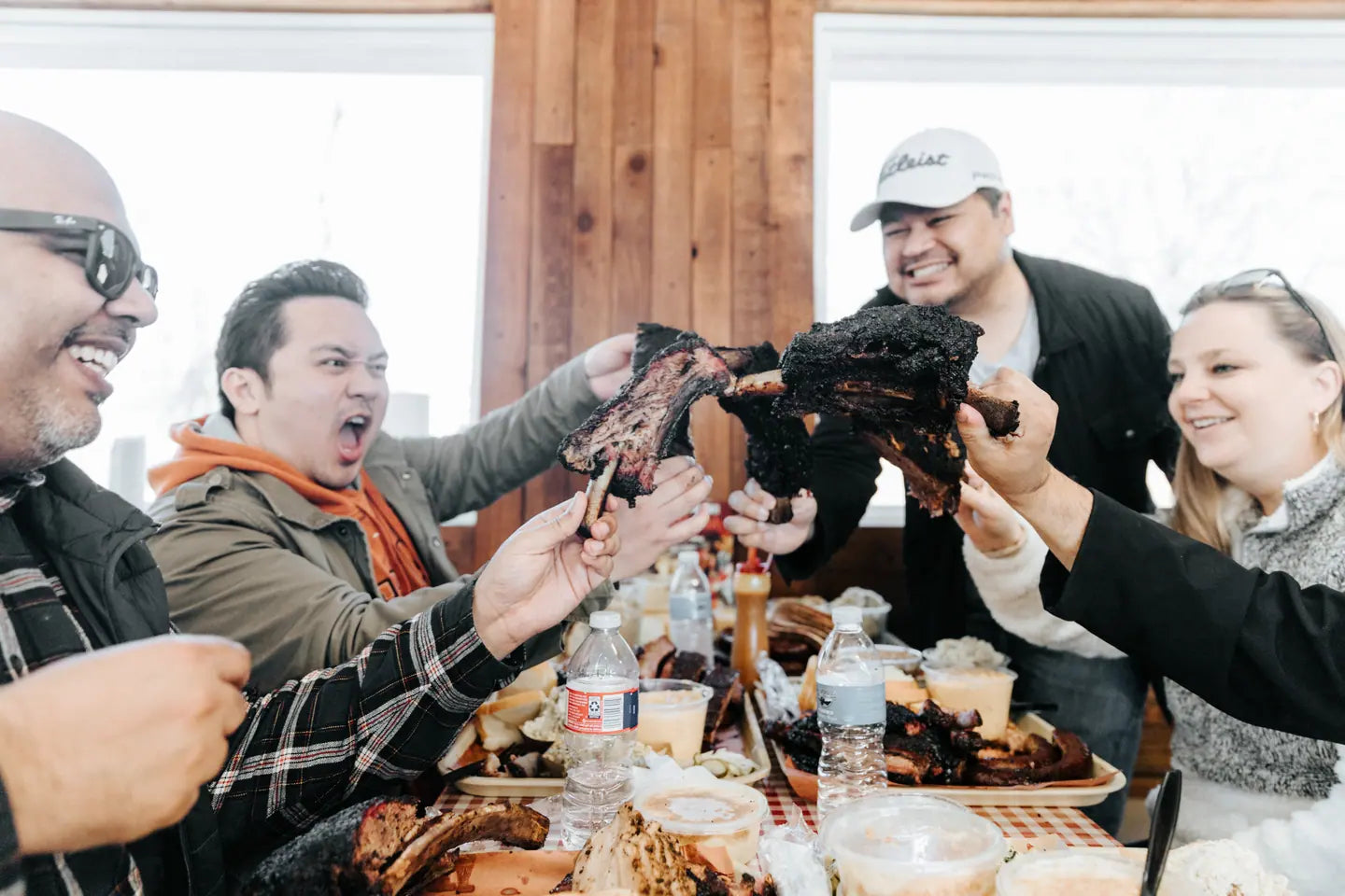 A table of guests laughing and raising a beef rib between them