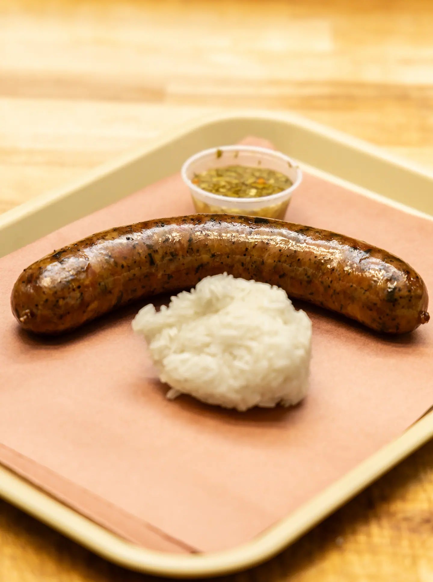 Lao sausage served on a tray with a scoop of sticky rice and a cup of dipping sauce