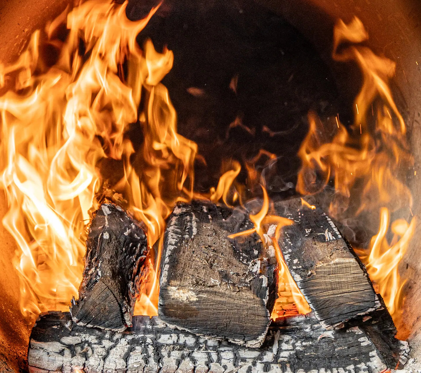 Flames climbing over split logs inside an open firebox