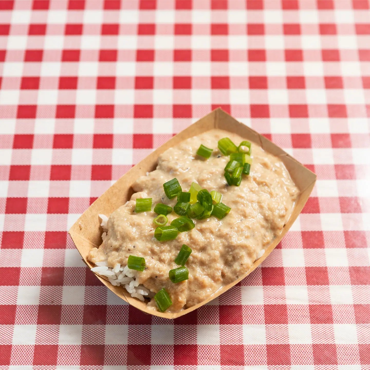 A boat of South Carolina pork hash topped with spring onion on a red gingham table
