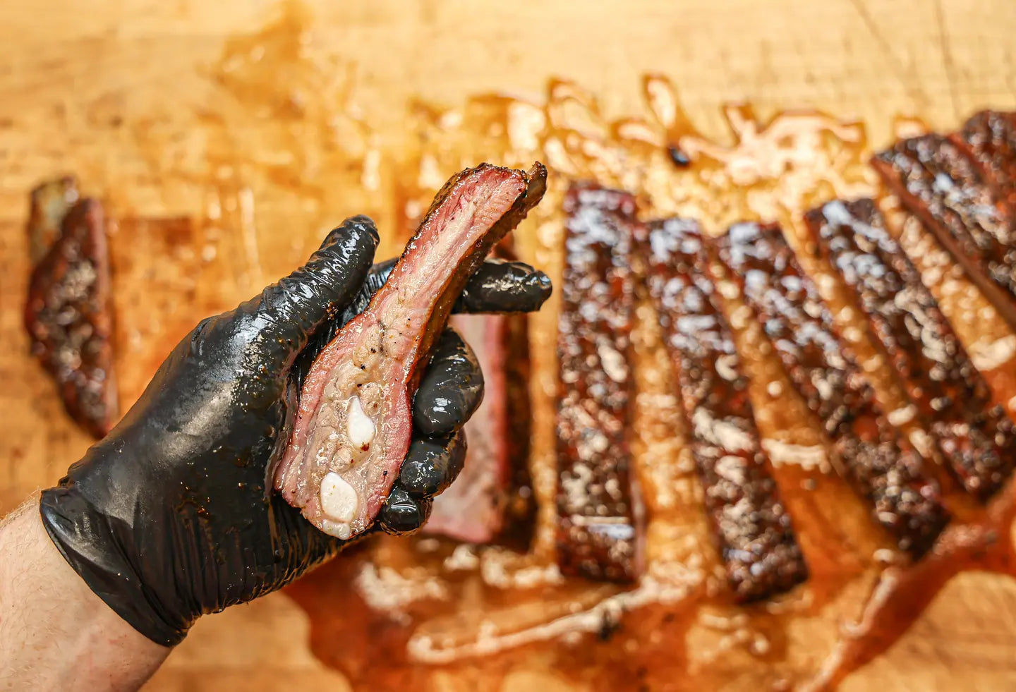 A gloved hand lifting one rib clear of a sliced rack, the cut face showing the meat pulling from the bone