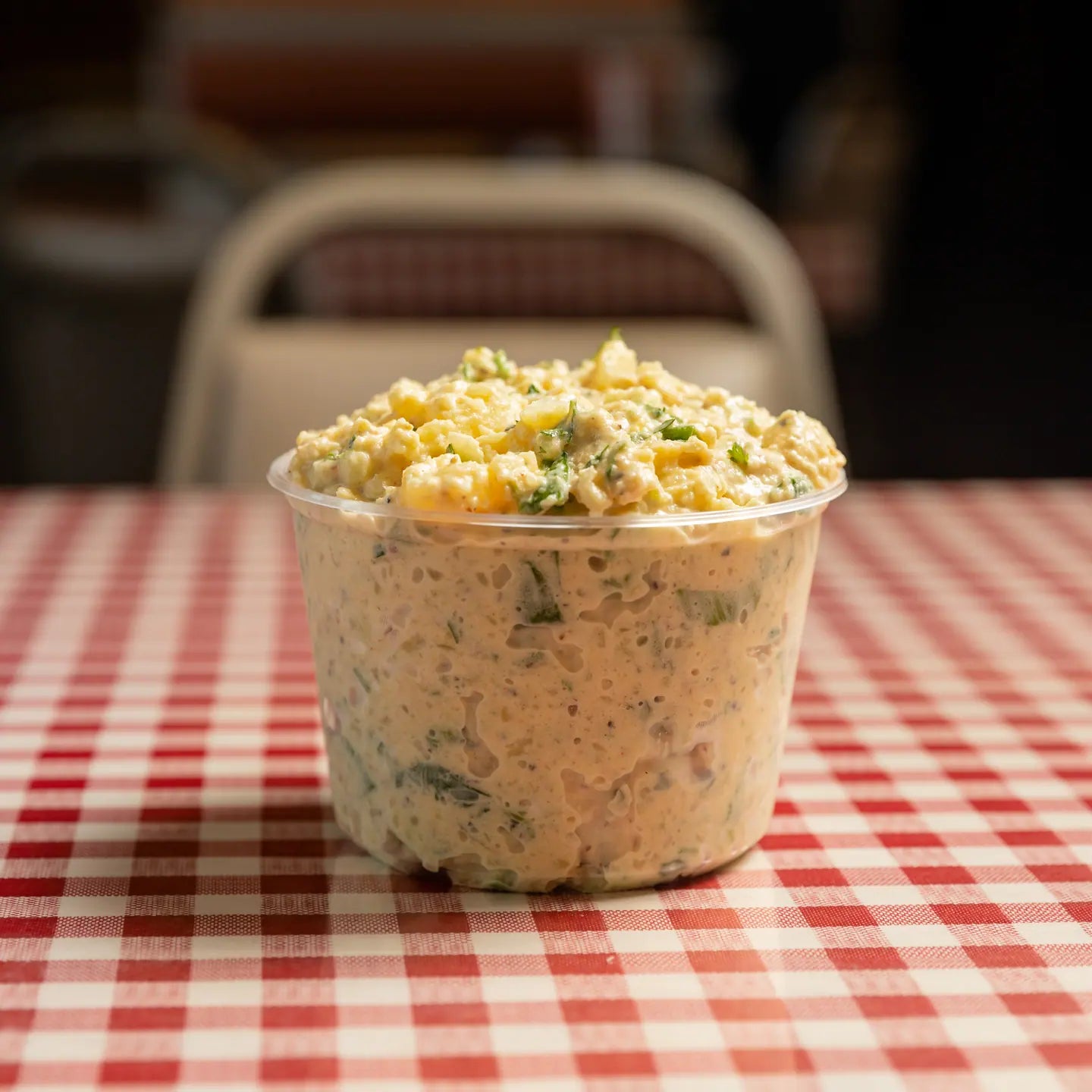 A cup of potato salad on a red gingham table