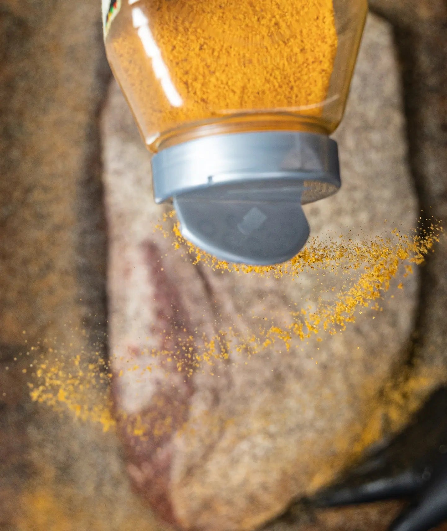 Goldee's rub pouring from its shaker onto a seasoned brisket