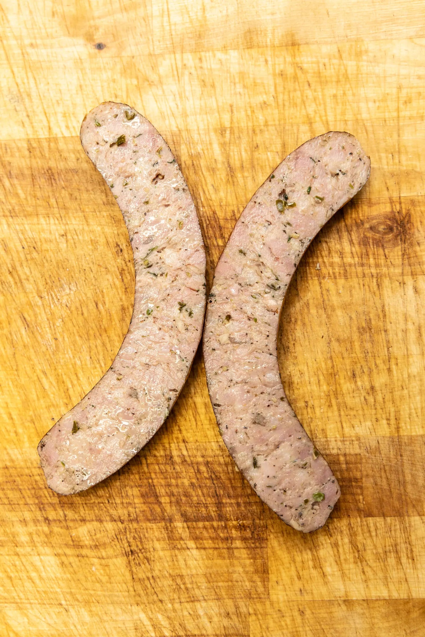 Two halves of a house sausage on a wooden board, the seasoned interior facing up