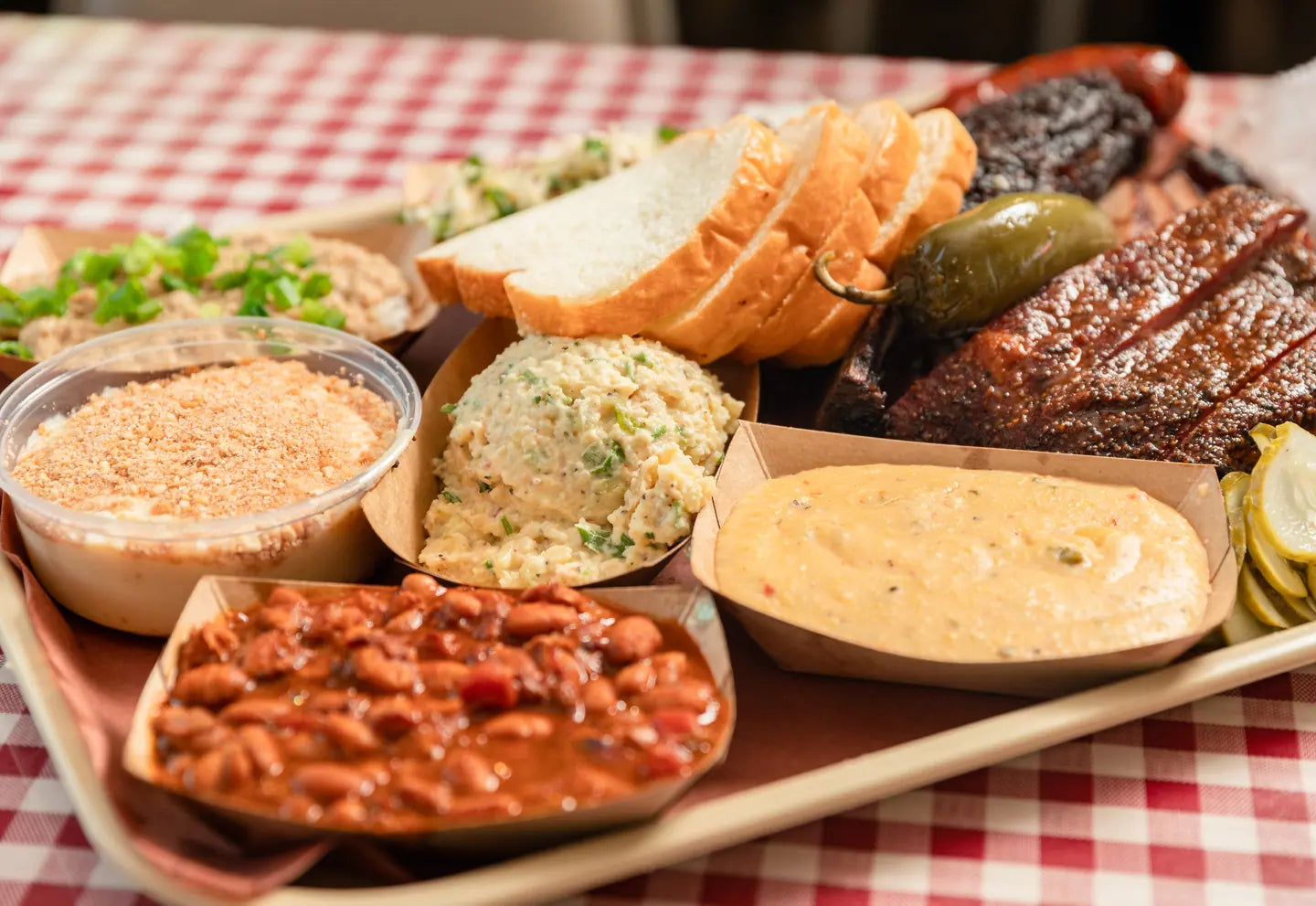 Beans, potato salad, slaw, bread and sausage laid out together on a tray
