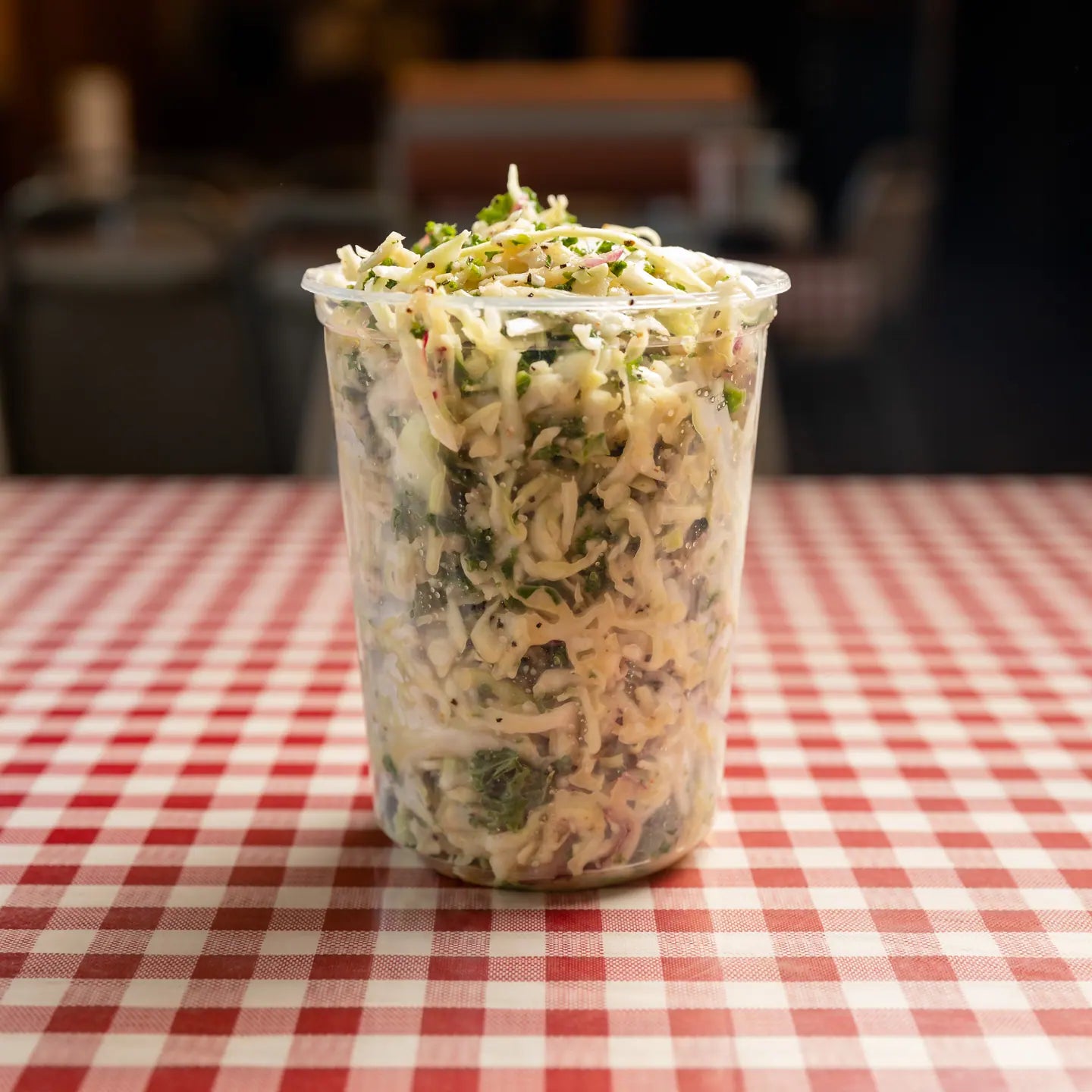 A cup of lemon kale slaw on a red gingham table