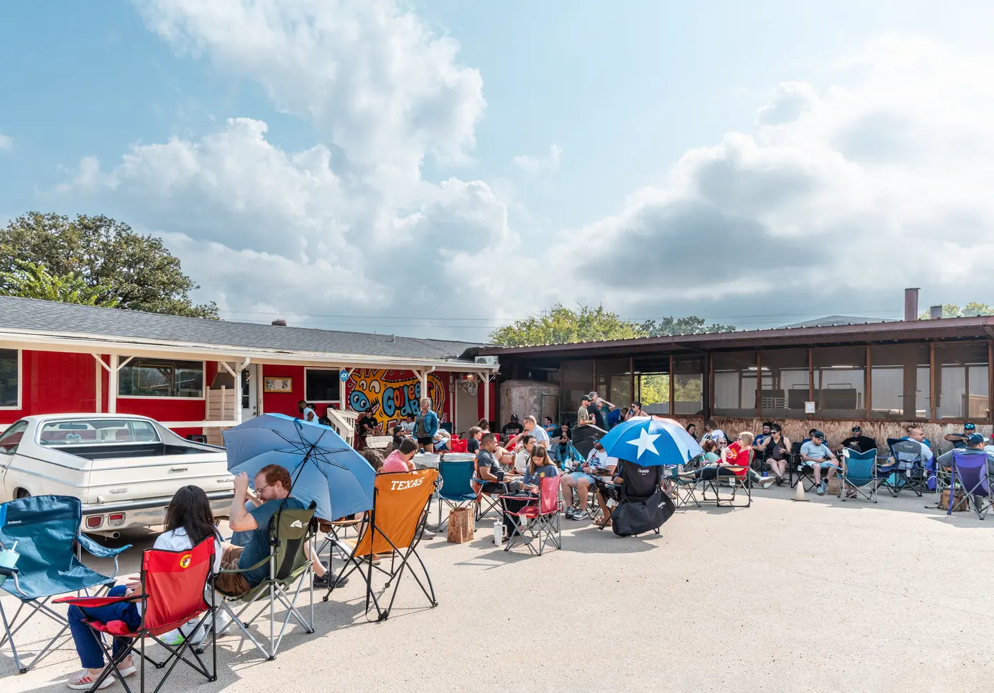 Customers waiting in lawn chairs and under umbrellas across the parking lot at Goldee's