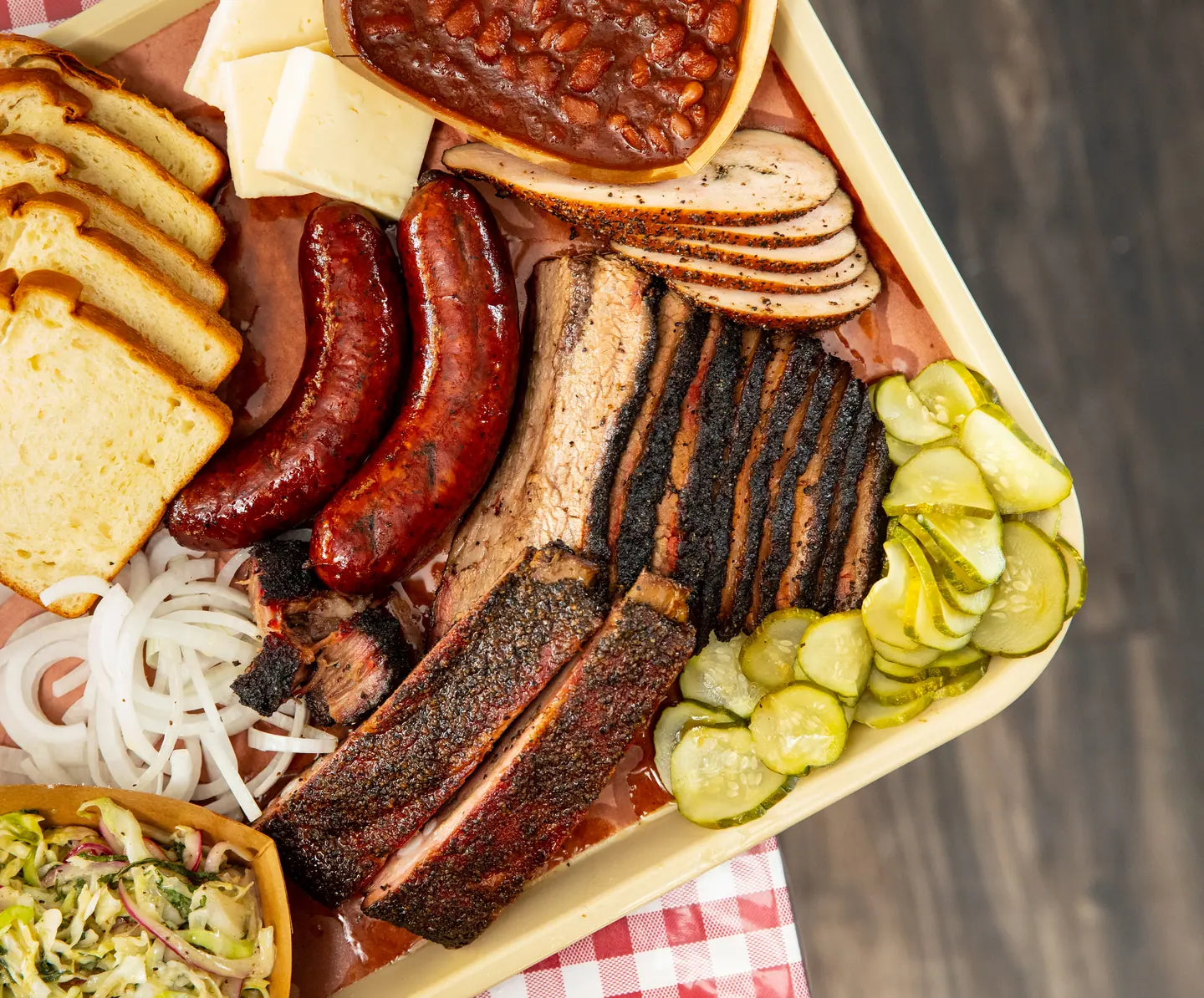 A loaded tray of brisket, ribs, sausage and sides on a wooden table, seen from above