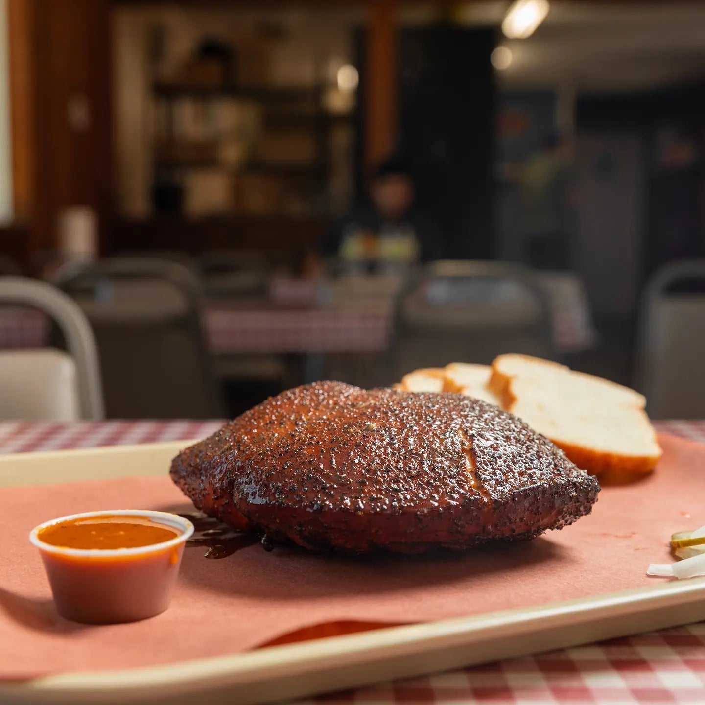Sliced smoked turkey breast on a tray with bread, pickles and a cup of sauce